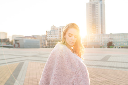 Fashionable street portrait of a model in pink clothes on the street in the background of the sunset. Cute girl in pink dress poses on the camera at the background of the evening city landscape.の写真素材