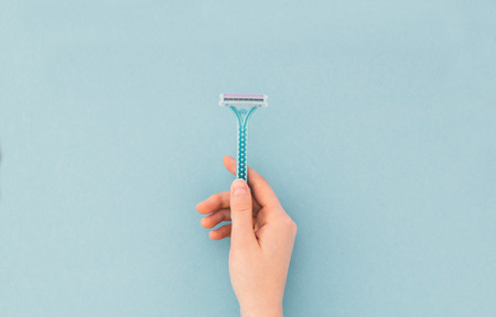 Woman holds a razor in her hand on a blue background, a view from above. Copyspace. Flat layの写真素材