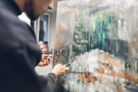 Photo of a talented artist with a knife palette and garnish in his hands creating a picture of oil. Painting Concept. Paint the paint on the host using a knife palette. Creative process of creating a picture.の写真素材