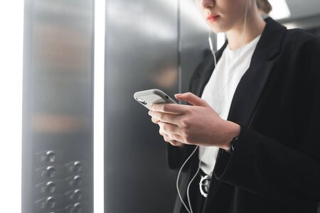 Close up photo of a busy young woman using smartphone in the elevator. Ambitious office worker...