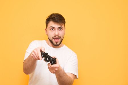 Portrait of a bearded man with a gamepad in his hands,plays console games on a yellow background,...