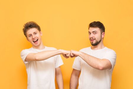 Studio shot of o bearded man and teenager, give fist bump, agree to work together, wear a white T-shirt, look at the camera and smile on the yellow background.の写真素材