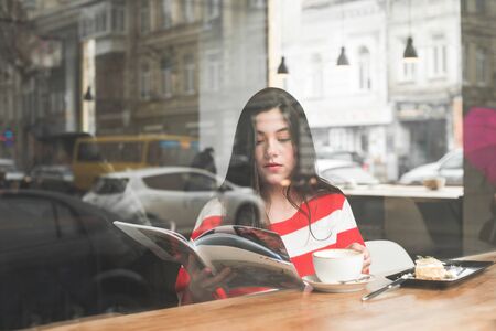 Portrait of an attractive girl sitting in a cafe with a magazine in her hands,reading,drinking...