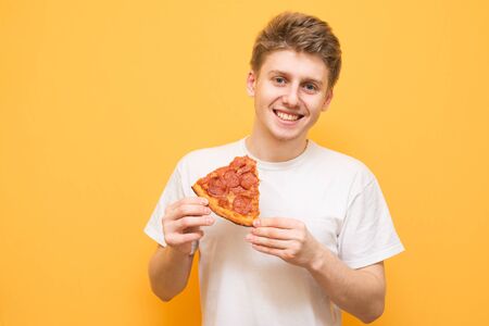 Portrait of a smiling guy dressed in a white T-shirt isolated on a yellow background, holding a...
