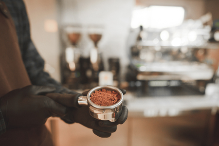 Barista holds in his hands a holder with fresh ground coffee, close. Cooking coffee in the coffee shop. Coffee culture concept. Backgroundの写真素材