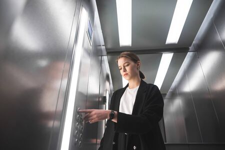 Beautiful young businesswoman wearing black suit is using elevator. Ambitious female office worker...