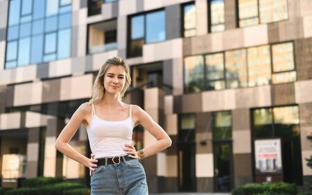 Street portrait of an attractive girl in a white T-shirt and jeans stands on the street against the...