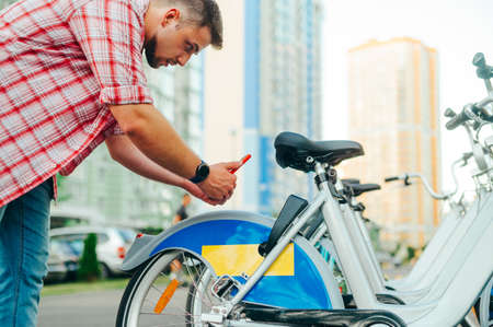 Man in a shirt scans the qr code on a bicycle and wants to rent a bicycle. Guy takes a sharing bike...