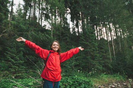Attractive and happy tourist girl raising her hands up to the sky feeling cheerful in the mountain...