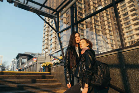 Street photo of two girls standing on stairs on urban background, looking and posing in camera,...