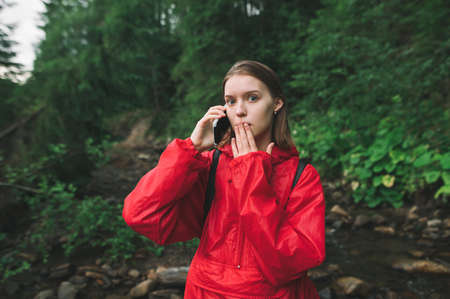 Young female tourist is in mountain forest near the river feeling scared and shocked, talking on the...