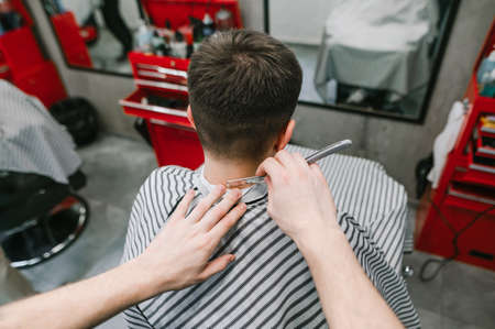 First-person photo of a barber shaving a client's neck with a straight razor at a men's hair salon. Men's hairdresser creates stylish men's hair with a straight razor. Barber shop concept.の写真素材