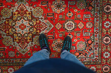 Man stands on the carpet and takes a photo of his feet. Fashionable sneakers on her feet and wears jeans. Background Photo of legs with sneakers and jeans, top view, standing on the carpet.の写真素材