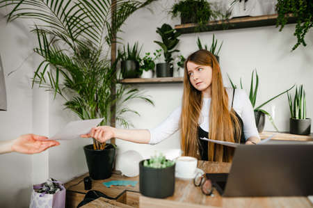 Smart lady sits at a coffee table with a laptop and documents in her hands, looks away and gives...