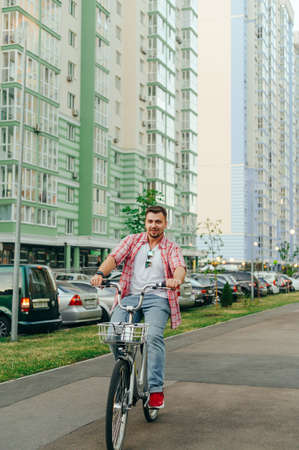Positive man with a beard rides a city bike around the city with a smile on his face. Cheerful man rides a bicycle with a shering on the street of the town. Bicycle rentalのeditorial素材