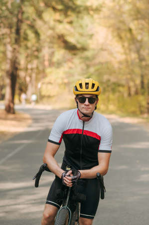 Portrait of serious young man cyclist in helmet and sunglasses standing with cyclist in autumn...