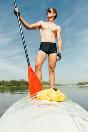 Background. Abstract blurred photo. Young man with an oar in his hand stands on a sup board. Vertical.の写真素材