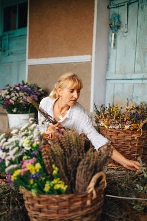 Portrait of an attractive female florist creates a bouquet of dried flowers with a serious face. Decorator makes a composition of dried flowers. Verticalの写真素材