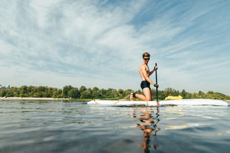 Handsome young man with a sports torso calmly paddles on a sup board on the river. The guy swims on...