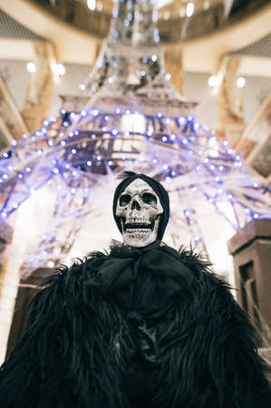 Close photo of a skeleton of a woman in dark clothes on in a room decorative for Halloween. Background. Vertical. Skull in a black kerchief on a background of garlands.の写真素材
