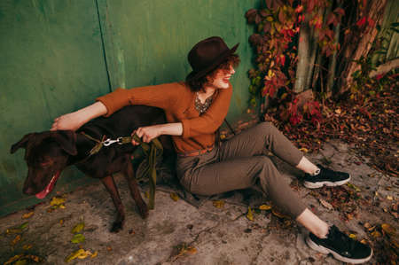 Happy lady in trendy vintage clothes sits on the ground in the yard of a country house and plays...