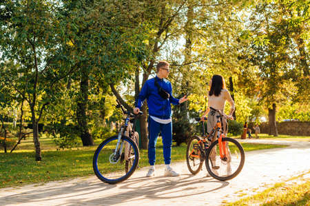 Couple of stylish young men in sportswear standing with bicycles in autumn parquet talking. Couple relaxing in the park on bicycles.の写真素材