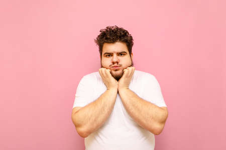 Cute curly fat man with beard posing for the camera on a pink background, looking into the camera...