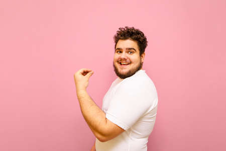 Portrait of a joyful fat guy on a pink background, emotionally happy to win and looking into the camera with a smile on his face. Happy overweight joyful man isolated on pink.の写真素材