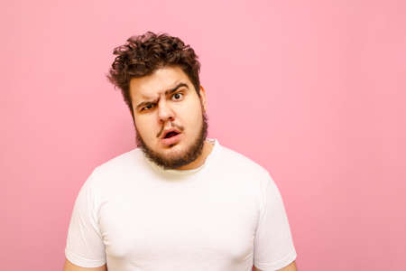 Closeup portrait of a funny surprised fat man with beard and curly hair on a pink background, looks into the camera with a look of astonishment. Surprised overweight guy looks into the camera.の写真素材