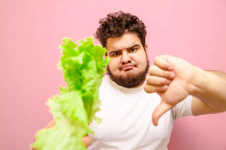 Closeup portrait of a funny fat man with lettuce in his hands on a pink background, looks into the...