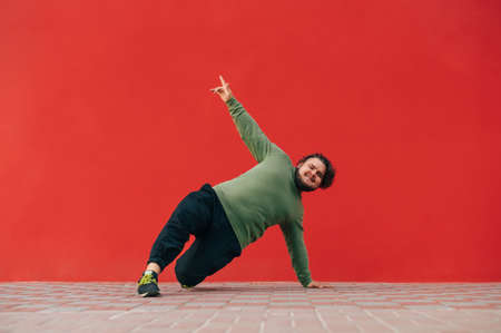 Positive overweight young man shows a dance performance on the street against the backdrop of a red...