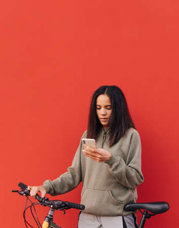 Attractive woman in casual brunette clothes enjoys a smartphone on a red background. Vertical.
