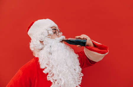 Santa Claus drinking cola from a bottle on a red background. Christmas and New Year.の写真素材