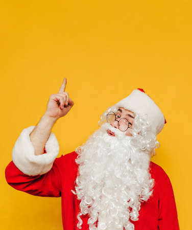 Santa Claus isolated on yellow background, looking at camera and showing thumbs up on copy space. Vertical.の写真素材