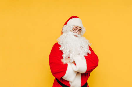 Happy man in santa claus costume stands on yellow background and looks at camera with smile on face. Isolated. Christmas and new yearの写真素材