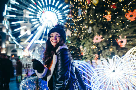 Happy lady standing in the center of the city at Christmas with a lighted sparkler in her hands on...