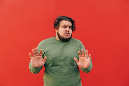 Attractive overweight charismatic young guy is expressing a stop gesture by showing his palms,...