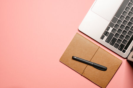 Colorful layout composition with a gray laptop with a black keyboard, brown notepad, and a pen on a...
