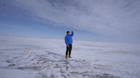 A man in a blue jacket stands on the frozen lake and looks at the horizon.の写真素材