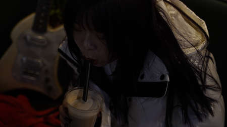 Young asian woman in white hoodie drinking milkshake while sitting in carの写真素材