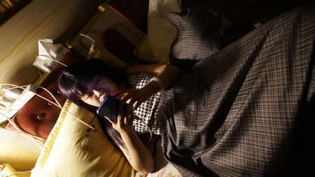 Young asian woman using mobile phone in the bed at night.の写真素材