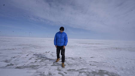 A man in a blue jacket and jeans walks along the frozen lake. A man walks along the frozen lake.の写真素材