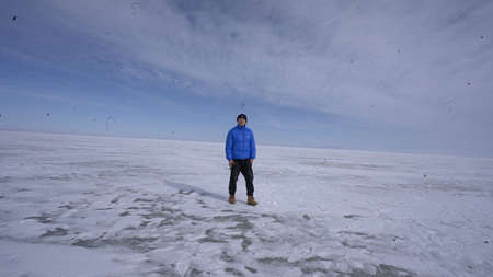 A man in a blue jacket walks along the frozen lake. A man walks on a frozen lake.の写真素材