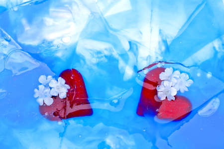 Two red glass hearts are covered by colored broken iceの写真素材
