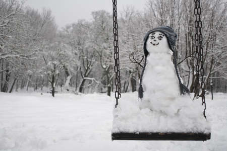Cute snowman on the swing at winterの写真素材
