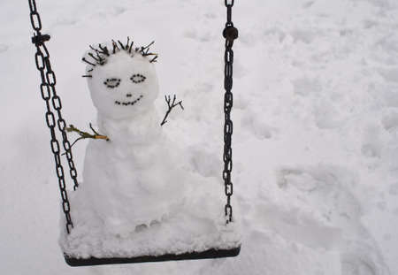 Cute snowman on the swing at winterの写真素材