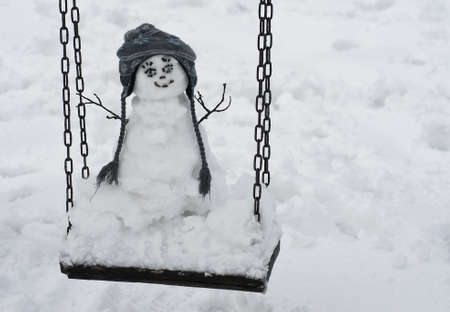Cute snowman on the swing at winterの写真素材