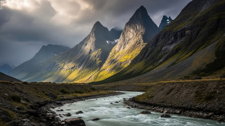 A scenic landscape showcases a flowing river winding through a valley, flanked by towering, rugged mountain peaks under a dramatic, overcast sky. The image displays contrasting light and shadow, highlighting textures and forms. Suitable for various editorial and commercial projects, the image conveys a sense of grandeur and natural beauty.の素材