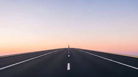 An asphalt road extends towards the horizon under a gradient sky transitioning from orange to blue. The composition features a symmetrical perspective with white road markings. This image, with its clean lines and vibrant colors, is suitable for various commercial applications including advertising and design projects.の素材