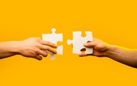 Two hands trying to connect couple puzzle piece on yellow background. Teamwork concept. Holding puzzle. Closeup hand of connecting jigsaw puzzle. Business solutions, success and strategy conceptの写真素材